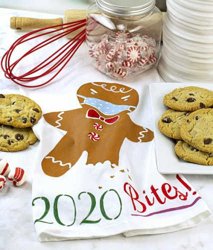 A tea towel with a gingerbread man wearing a face mask that says 2020 bites
